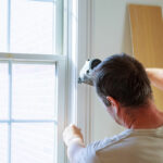 Carpenter using nail gun to moldings on windows, framing trim, with the warning that all power tools have on them shown illustrating safety concept