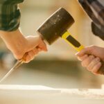 Closeup of unrecognizable carpenter hitting nail with hammer while working in joinery, copy space